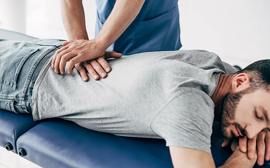 Man Lying Face Down On Blue Table Receiving Chiropractic Adjustment