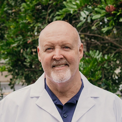Chiropractor John Warren Smiling Outdoors In Lab Coat
